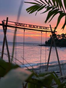 una puesta de sol en la playa con un cartel que lee la puesta de sol resort en Sunset Beach Resort Weh en Sabang