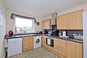 a kitchen with wooden cabinets and a washer and dryer at Caledonia Netherhills Apartment in Aberdeen