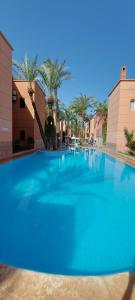 a large blue swimming pool with palm trees in the background at Les Riads Nour Resorts- Marrakesh Escape in Marrakesh