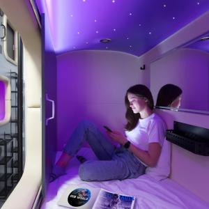 una mujer sentada en una cama en una habitación púrpura en Capsule Hotel Constellation 89 en Leópolis