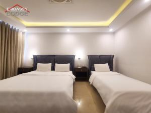 2 Betten in einem Hotelzimmer mit weißer Bettwäsche in der Unterkunft Embassy Lodge in Islamabad
