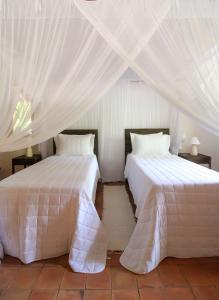two beds in a room with white curtains at Pousada Outeiro in Praia do Espelho