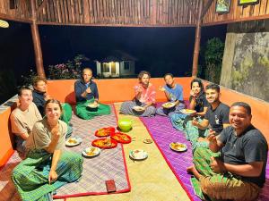 een groep mensen die op de vloer zitten te eten bij Sun Rice Homestay in Ruteng