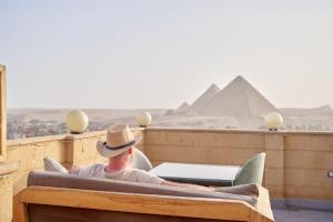 Gardenia Apartment Pyramids View في القاهرة: رجل يرتدي قبعة راعي بقر يجلس في سرير عند الاهرامات