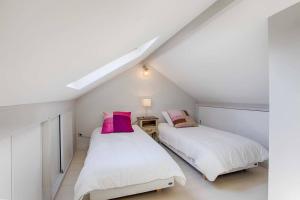 two beds in a attic bedroom with white walls and pink pillows at La Villa du Figuier Deauville quartier de l'église in Deauville