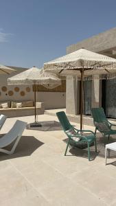 2 grüne Stühle und Sonnenschirme auf einer Terrasse in der Unterkunft Qash Villas in Jericho