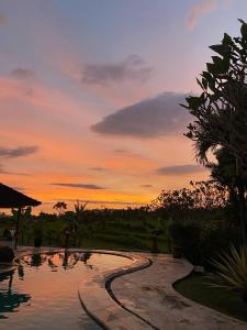 a swimming pool with a sunset in the background at Cabé Bali in Jasri