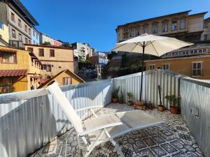 una silla blanca y una sombrilla en el balcón en Casa California Guesthouse, en Valparaíso