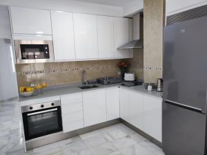 cocina con armarios blancos y nevera de acero inoxidable en Garu Apartamentos, en Fuengirola