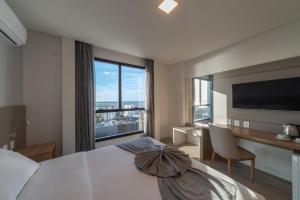 a bedroom with a bed and a desk and a large window at Hotel Laghetto Rio Grande in Rio Grande