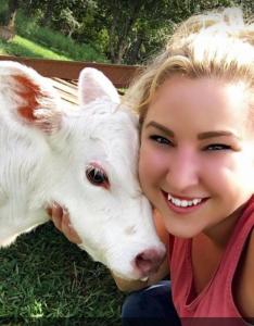 una mujer está sonriendo junto a una vaca blanca en Goin' Bonanza Glamping Ranch, en Hardy
