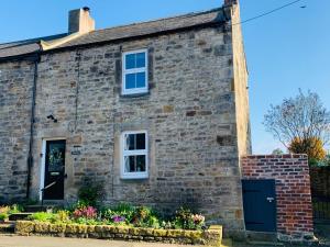 an old stone house with a blue door and flowers at Atte Combe Cottage in Acomb