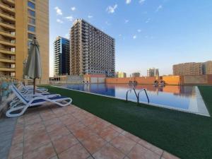 a pool with chairs and an umbrella on a building at Spacious Studio in IMPZ in Dubai