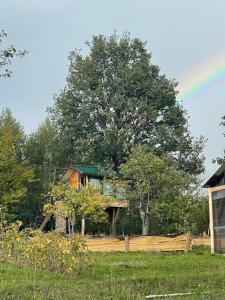 a house behind a fence with a rainbow in the sky at Langaland Glamping in Susenii Bîrgăului