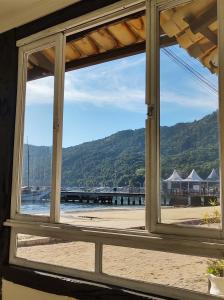 a window looking out at the beach and a pier at Pousada Mar Azul in Abraão