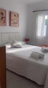 a bedroom with a large white bed with towels on it at APARTAMENTO CON ENCANTO EN RESIDENCIAL CON PISCINA in Cala'n Porter +8 photos