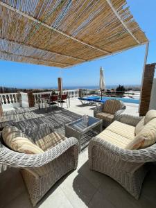eine Terrasse mit Korbstühlen, Tischen und einem Sonnenschirm in der Unterkunft Villa Delicia in Torrox