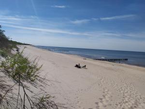 two people sitting on a sandy beach next to the ocean at Pink House Dziwnów 250 m od Morza in Dziwnów