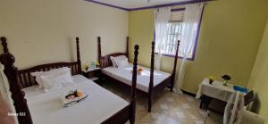 a room with two beds and a table and a window at Frankfurt Cottages in Mbale