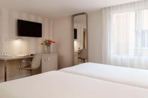 a bedroom with a white bed and a desk and a window at NH Madrid Balboa in Madrid