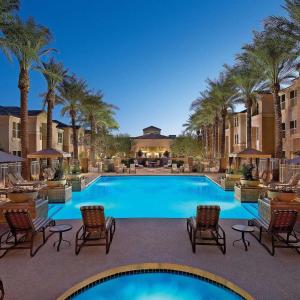 a large swimming pool with chairs and palm trees at Sonesta Suites Scottsdale Gainey Ranch in Scottsdale