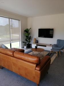 a living room with a brown leather couch and a tv at Purangi Beachhouse in Cooks Beach