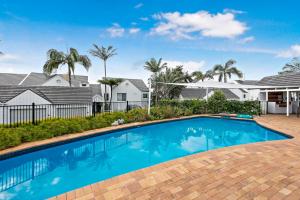 a swimming pool in front of a house with palm trees at Quarterdeck 18 in Lennox Head