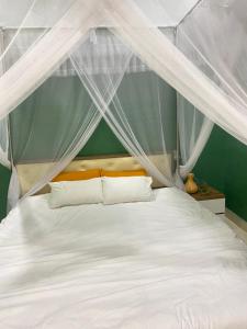1 dormitorio con cama con dosel, sábanas y almohadas blancas en Mon House, en Bao Loc