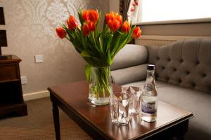 a vase of red tulips on a table with a bottle and glasses at Hamlet Hotels Maidstone in Maidstone