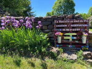 un cartel en un jardín con flores y una pared de piedra en La roulotte au fond du pré, en Coltines