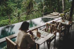a woman sitting at a table in front of a pool at Amora Ubud Boutique Villas in Ubud