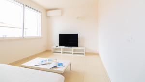 Habitación blanca con TV, cama y mesa. en Welcomely - Civico 48, en Torre Grande