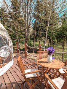 a wooden table with chairs and a vase of flowers on a deck at Medve Dome - Luxury Camping in the middle of nature in Vlăhiţa