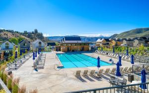 a swimming pool with lounge chairs and blue umbrellas at Chinook & Carriage House #2 in Chelan