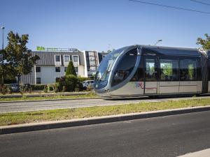 a train is traveling down a road next to a street at ibis Styles Bordeaux Aéroport in Mérignac