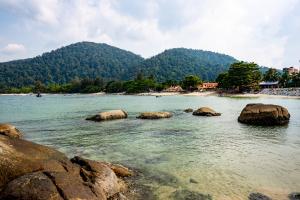 a body of water with rocks and mountains in the background at HyperTribe -Pangkor Holiday Home in Kampong Sungai Udang