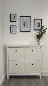 a white dresser against a white wall with three pictures at Madison Court Apartments in Hemel Hempstead