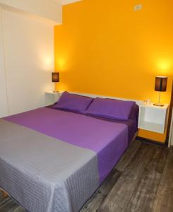 um quarto com uma cama com lençóis roxos e uma parede amarela em Corrientes em Mar del Plata