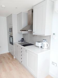a white kitchen with white cabinets and a sink at 'The Limes' - Air-Con Two Double Bedroom Holiday House with Private Garden in Kent