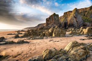 a sandy beach with rocks and the ocean at Hillside Chalet in Kilkhampton