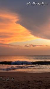 a sunset on the beach with a wave in the ocean at Villa Paradise Ocean in Bentota