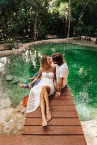 Un homme et deux femmes assis sur un quai dans un bassin d'eau dans l'établissement Nahouse Jungle Lodges, à Tulum