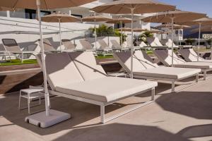 eine Reihe von weißen Stühlen und Sonnenschirmen auf einer Terrasse in der Unterkunft Servatur Hartaguna - Adults Only in Puerto Rico de Gran Canaria