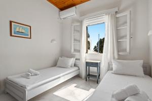 two beds in a white room with a window at Villa Kalomira in Spetses