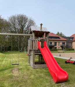 einen Spielplatz mit einer roten Rutsche und einer Schaukel in der Unterkunft Wohnen am Südstrand - Ferienwohnung 2 1 in Wyk auf Föhr