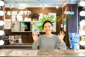 Una mujer sentada en una mesa con las manos en alto. en Guest House Shinagawa-shuku en Tokio