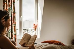a woman sitting on a bed reading a book at La Maison Montparnasse in Paris