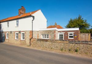 a white house with a brick wall next to a street at Cuckoo Cottage in Blakeney