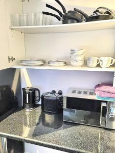 a kitchen counter with a microwave and dishes on shelves at Bishop Retreat in Bishop Auckland