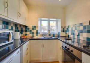 a kitchen with white cabinets and a sink and a window at Reeve Cottage in Blakeney
